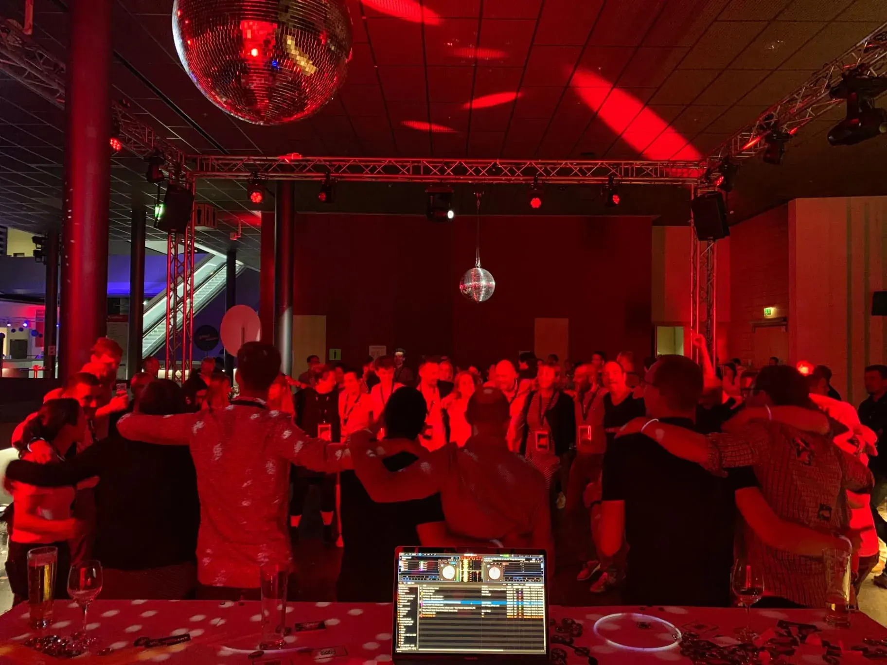 Volle Tanzfläche unter Discokugel im rot ausgeleuchteten Saal hinter dem DJ-Pult von Chris Force